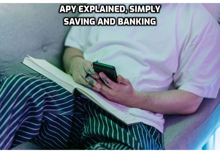 A real photo of a person reviewing a savings account on a phone at home, with a notebook and calculator nearby, with the headline APY Explained, Simply.