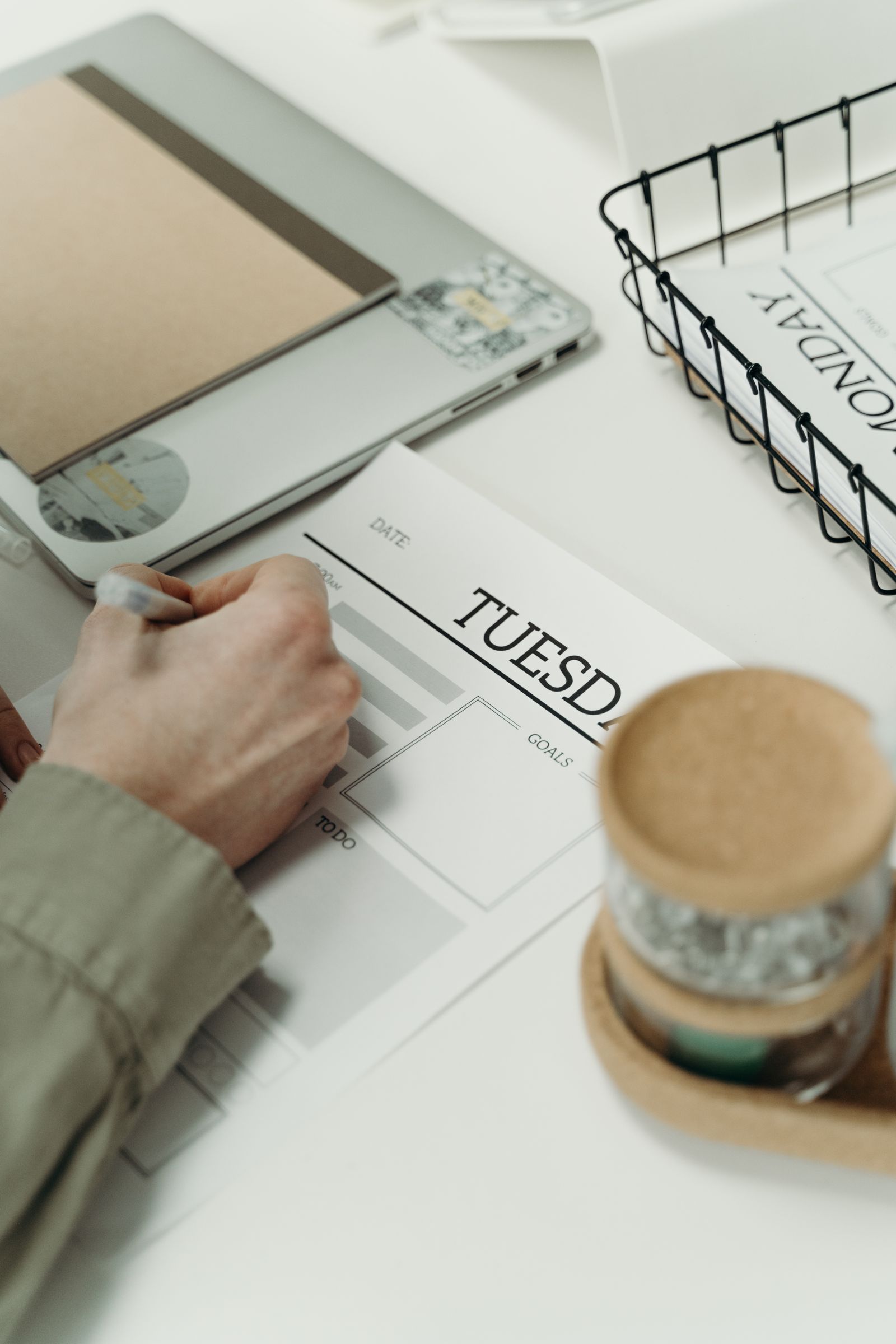 A person writing a weekly shopping list at a desk to stay within a grocery budget