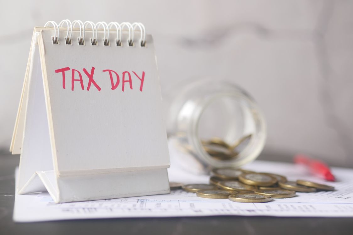 A real photograph of a wall calendar with months crossed off, next to a small savings jar