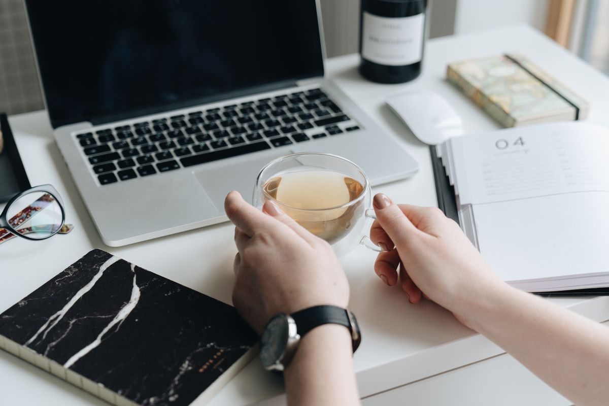 A freelancer working on a laptop in a clean home workspace, with a notebook and a cup of tea nearby