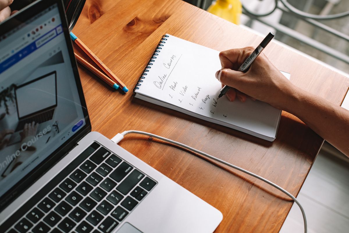 A person researching a company on a laptop, with a written checklist in a notebook beside the keyboard
