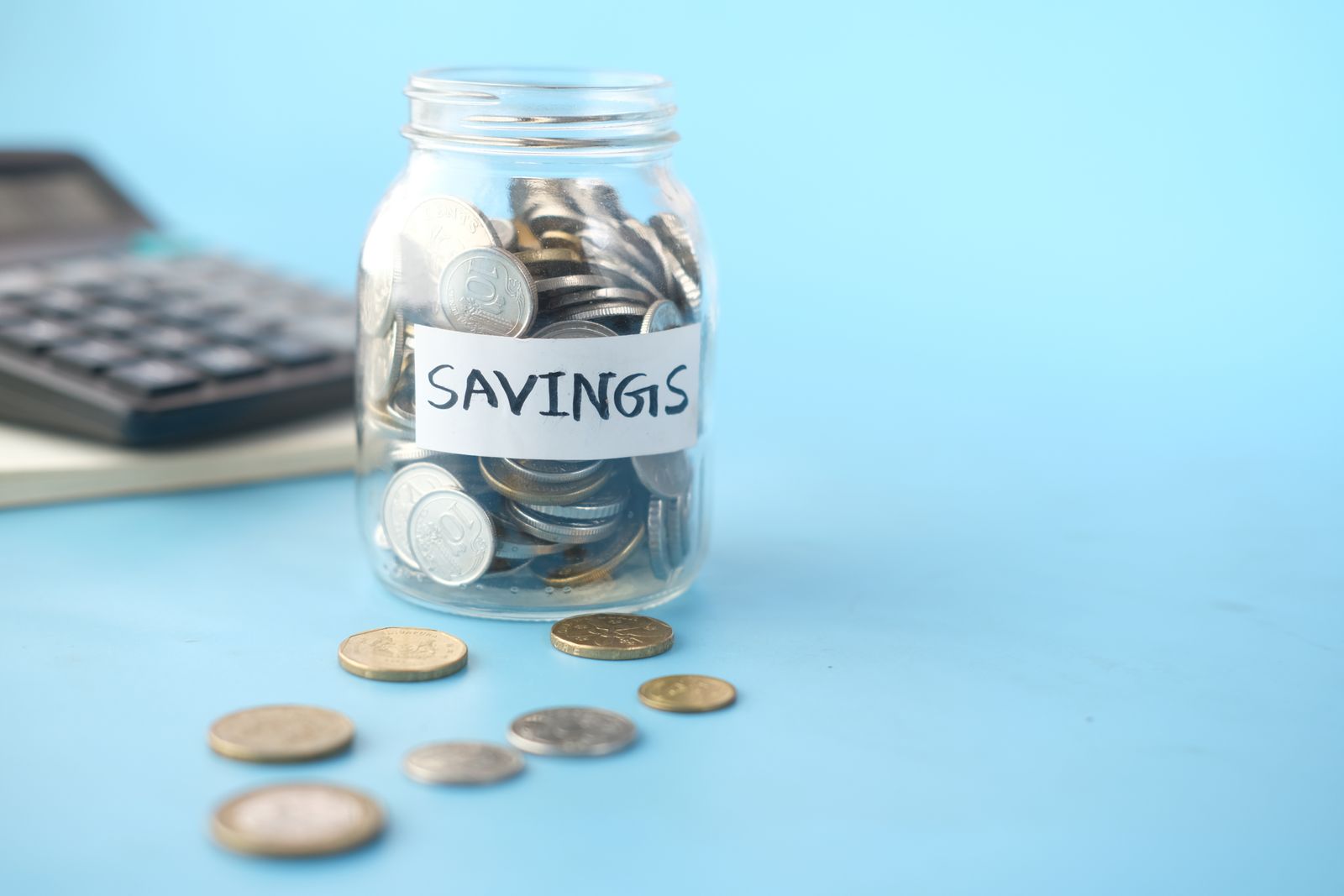 A savings jar with coins on a desk beside a notebook